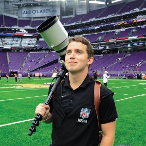 preson holding large camera lens with football field in background