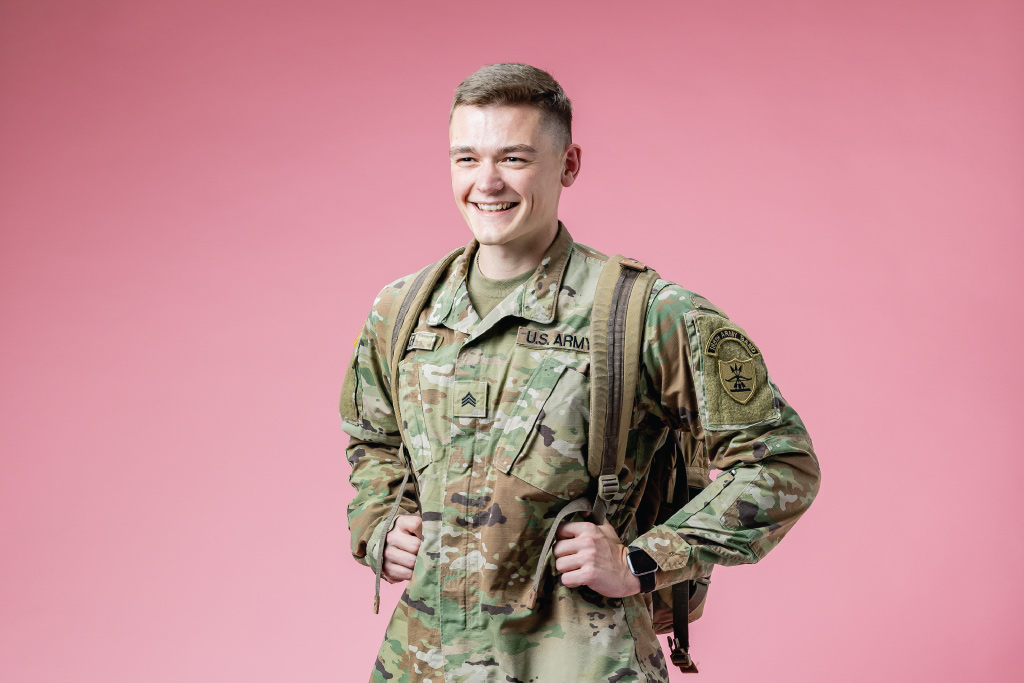 thomas wearing army uniform holding backpack on pink background